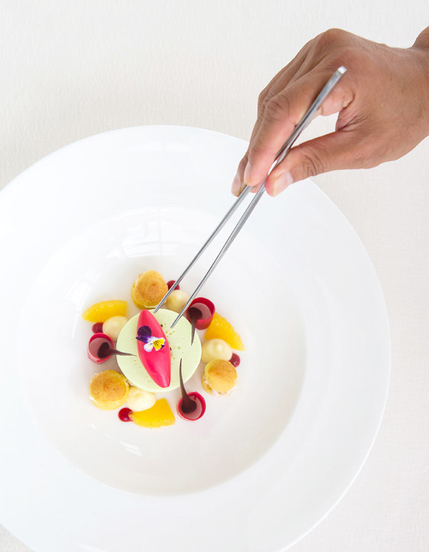 Tweezers placing a garnish in a white bowl