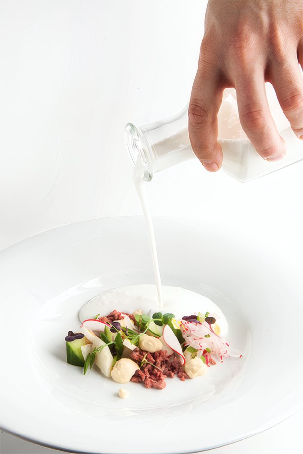 A chef pouring a sauce at the pass