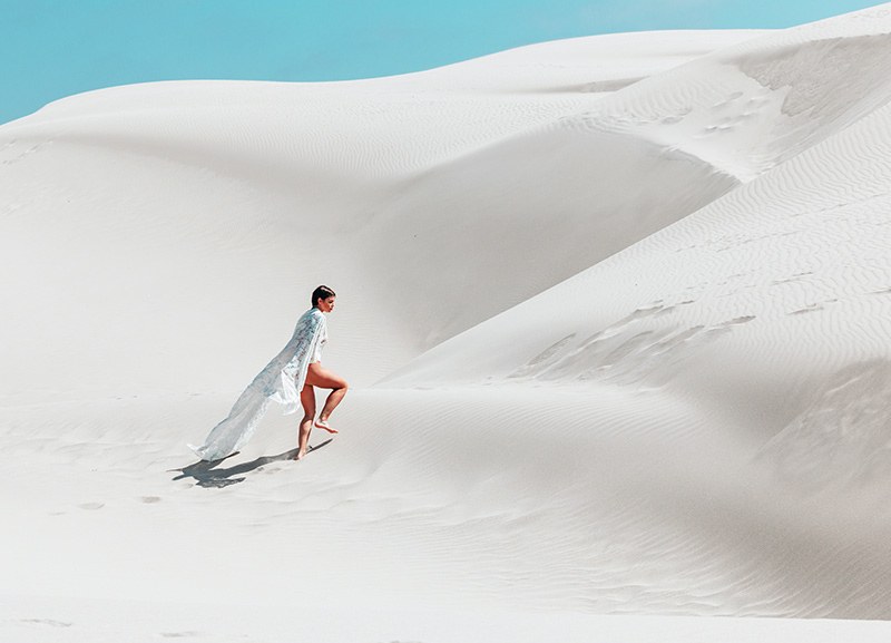A figure in white walking up a white dune