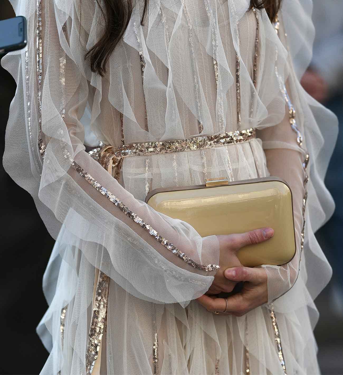 A woman in a sequinned dress holding a gold clutch