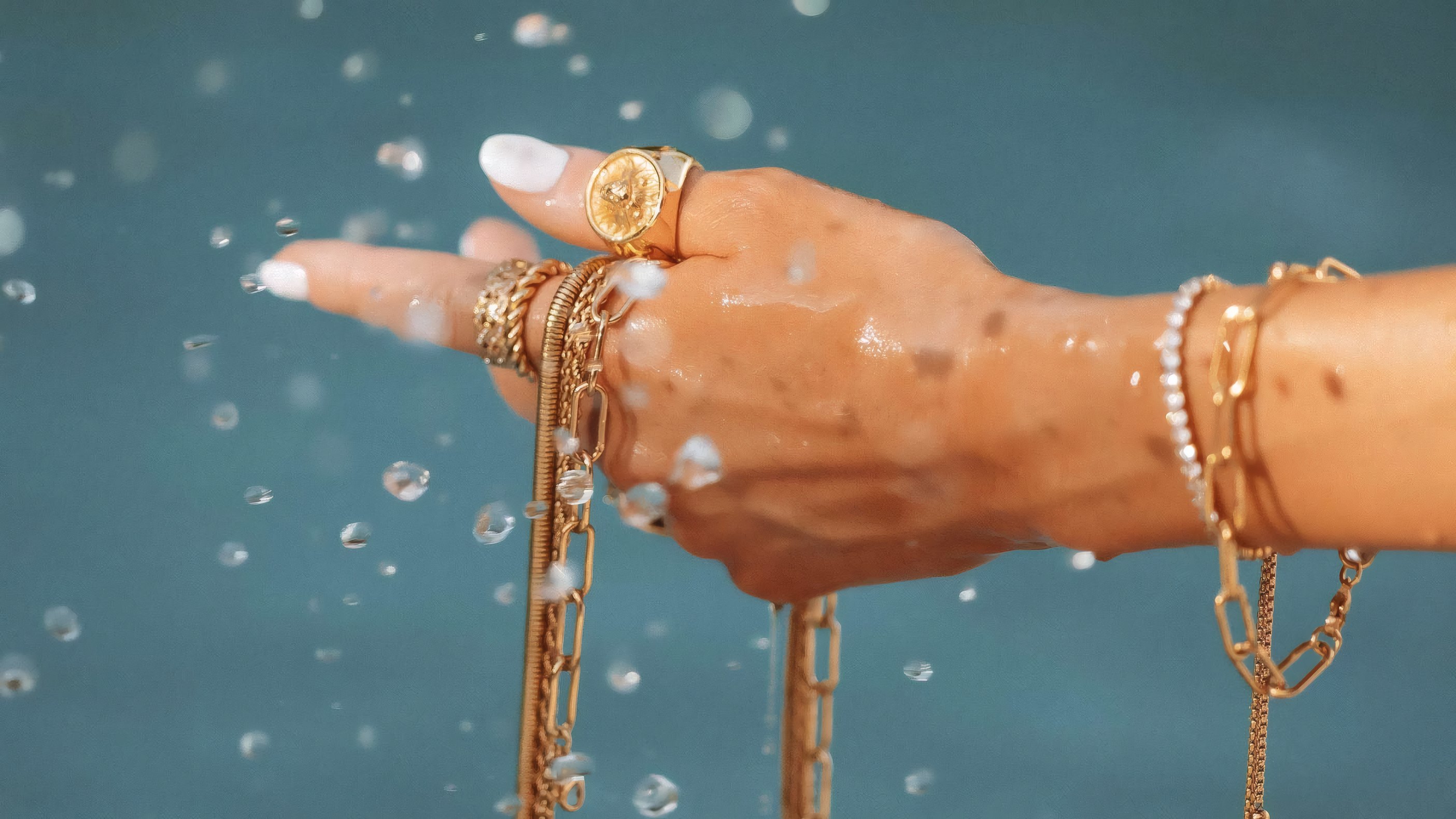 A hand in gold bracelets and rings lifted out of the water