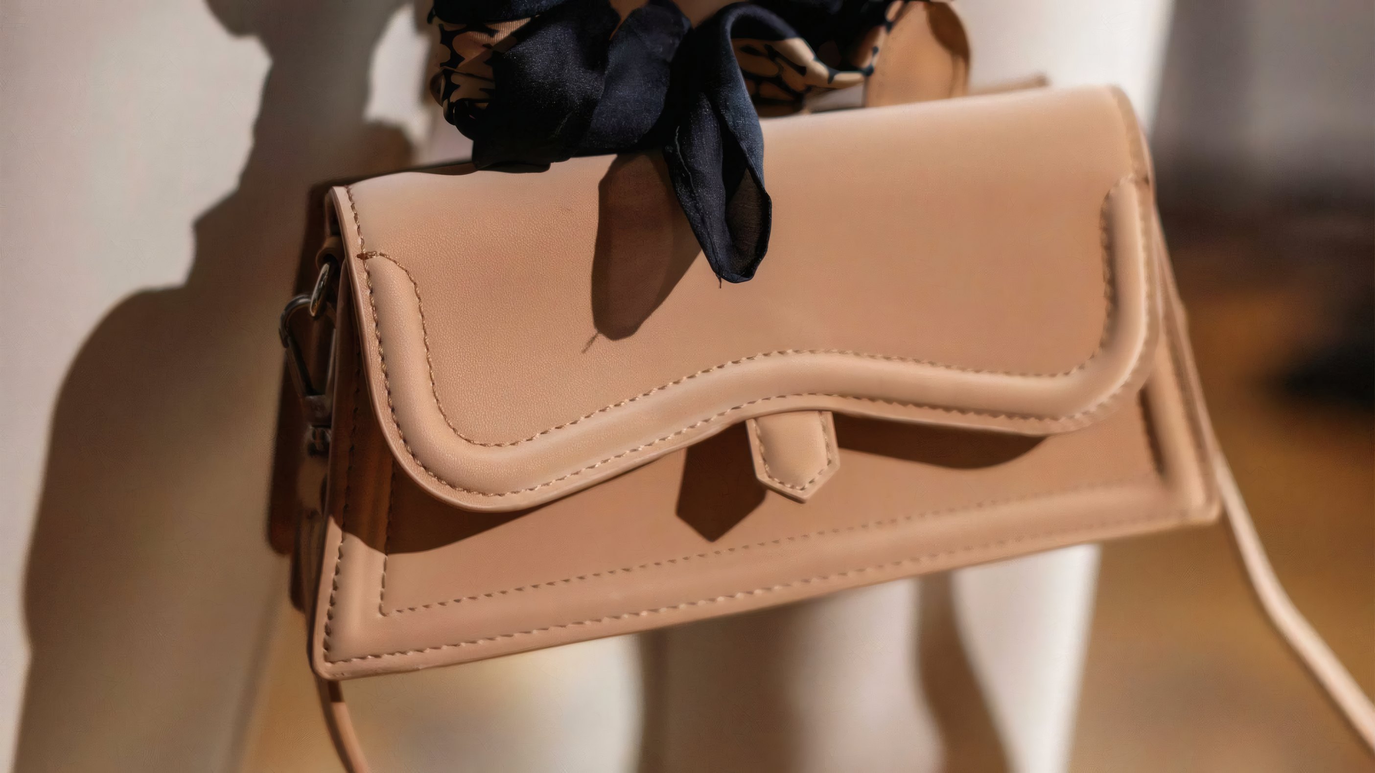 A tan leather bag tied with a black silk scarf