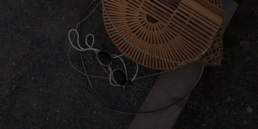 A straw bag and sunglasses on a dark table