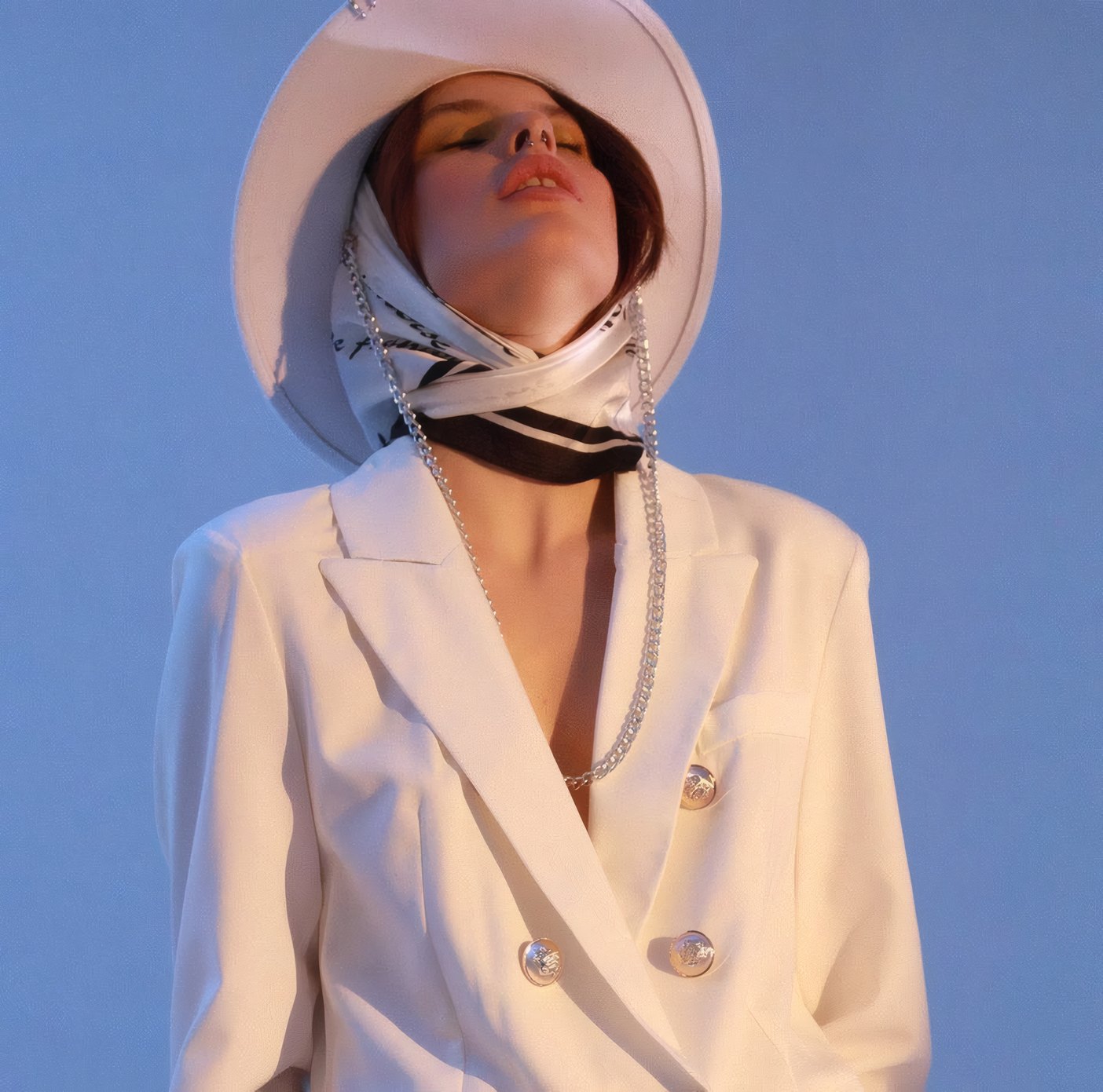 A woman in a white blazer and a silk headscarf against blue
