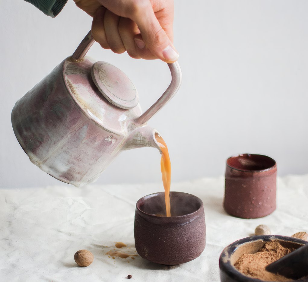 Tea poured from a stoneware pot into a dark clay cup