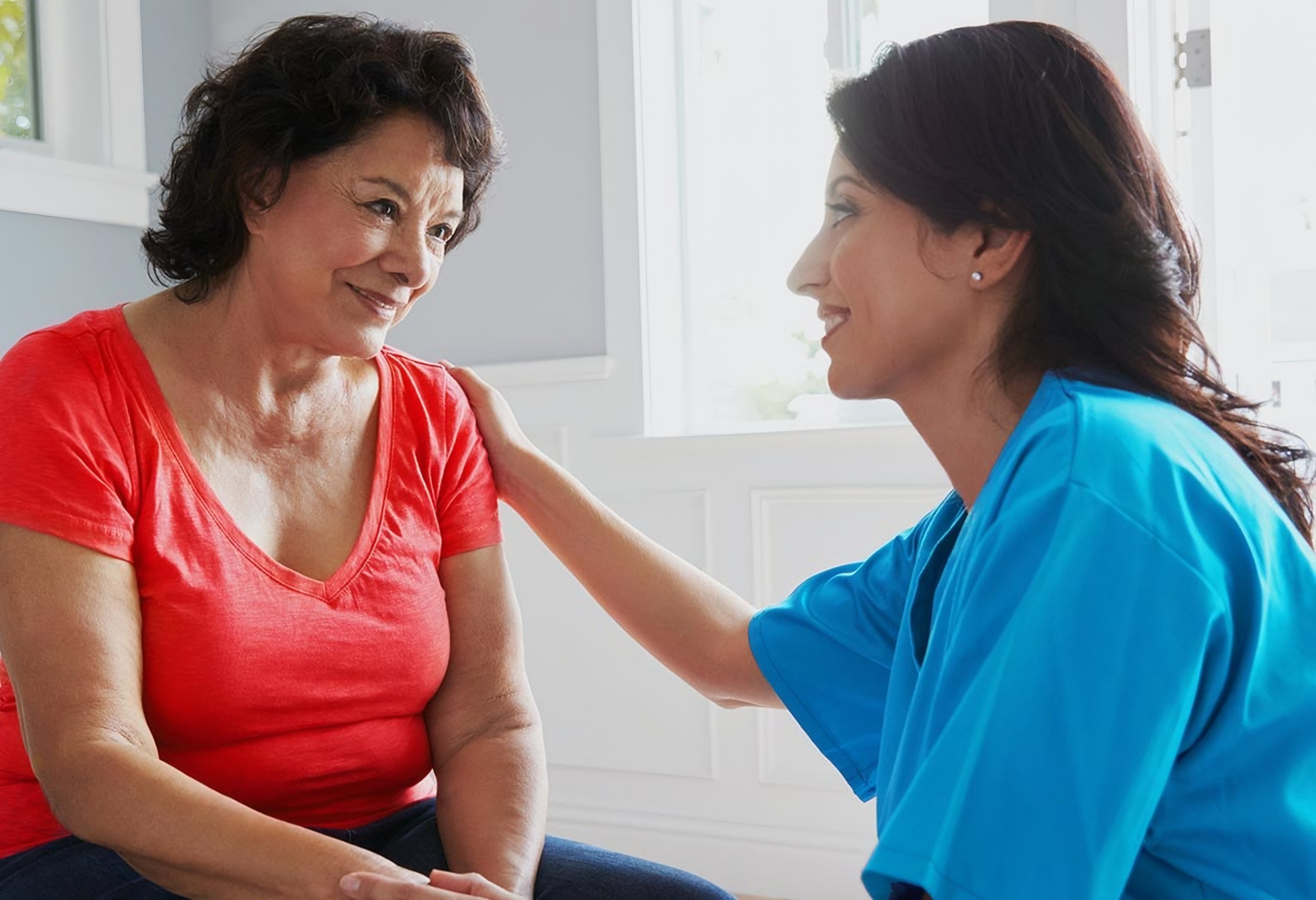 A nurse holds an older patient's hands during a home visit
