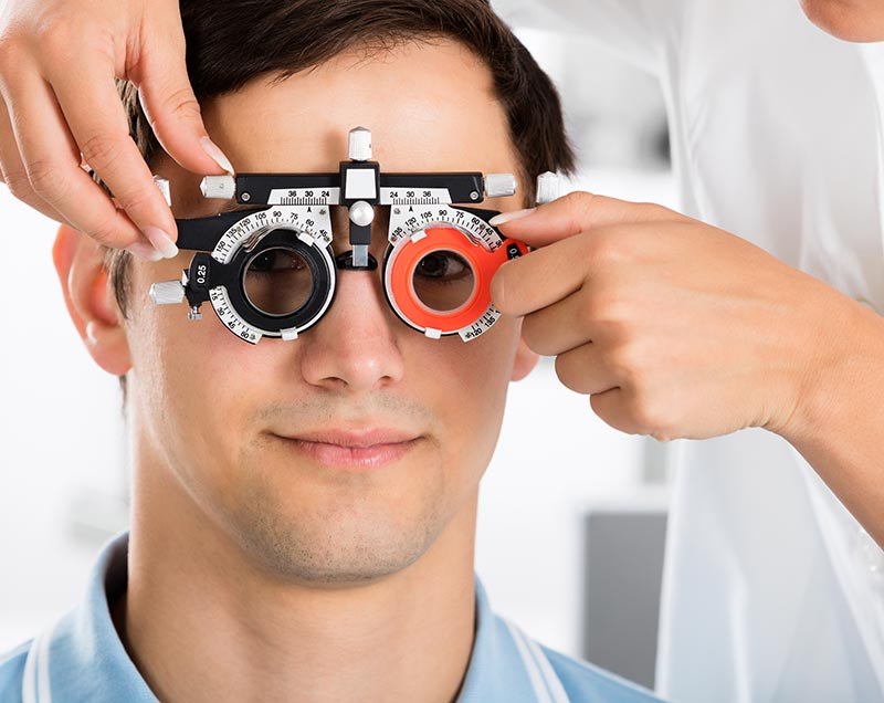 An optometrist checks a man's eyes with a trial frame