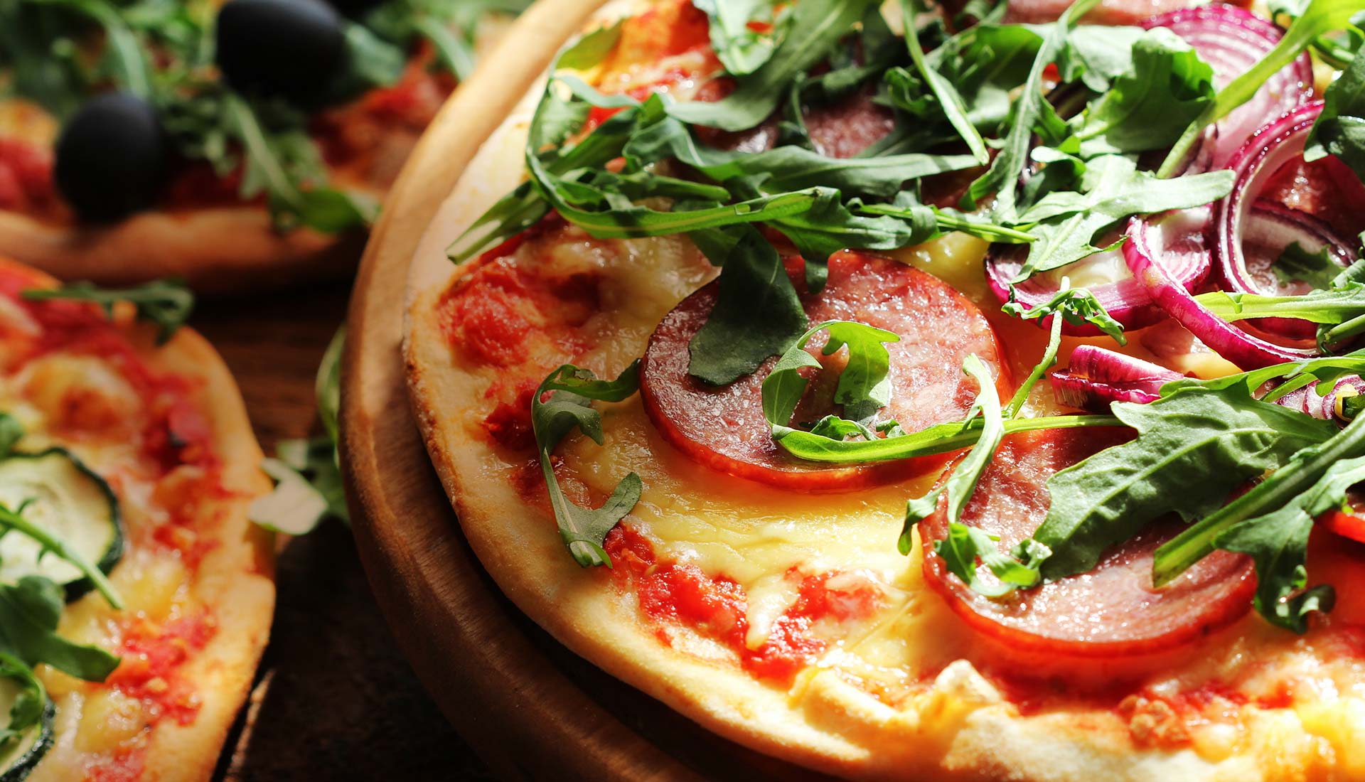 A wood-fired pizza with salami, rocket and olives