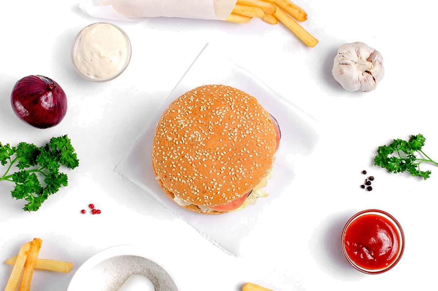 A burger bun surrounded by its ingredients from above