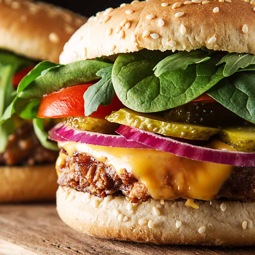 A burger with cheese, spinach and red onion