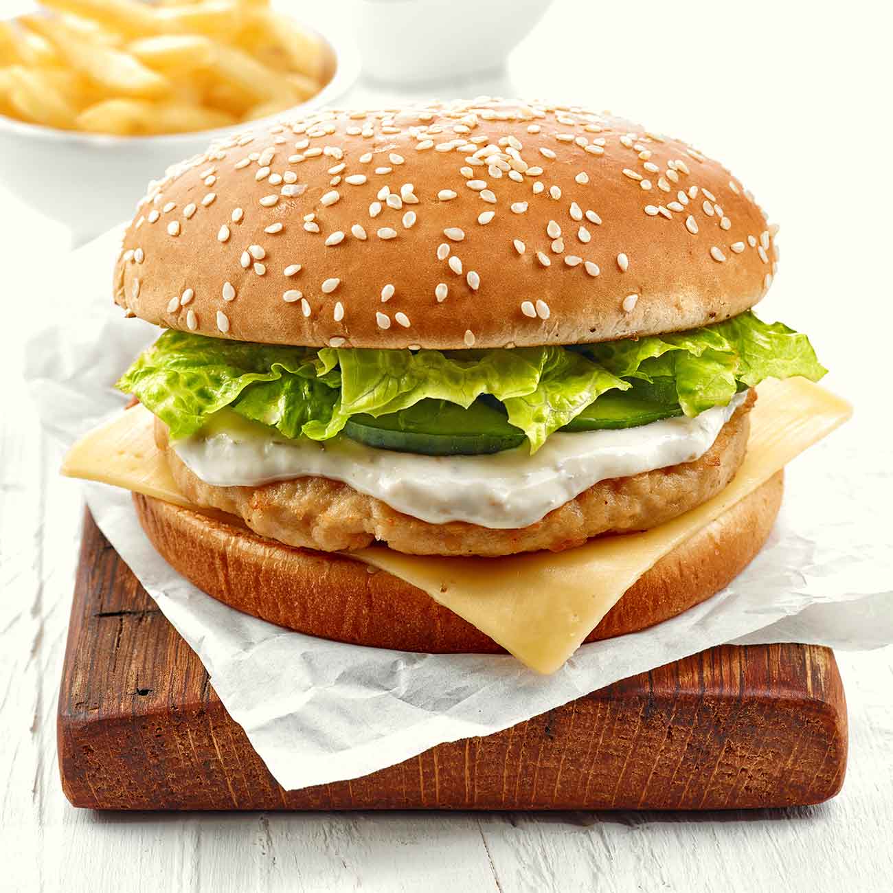 A chicken burger with cheese on a wooden board