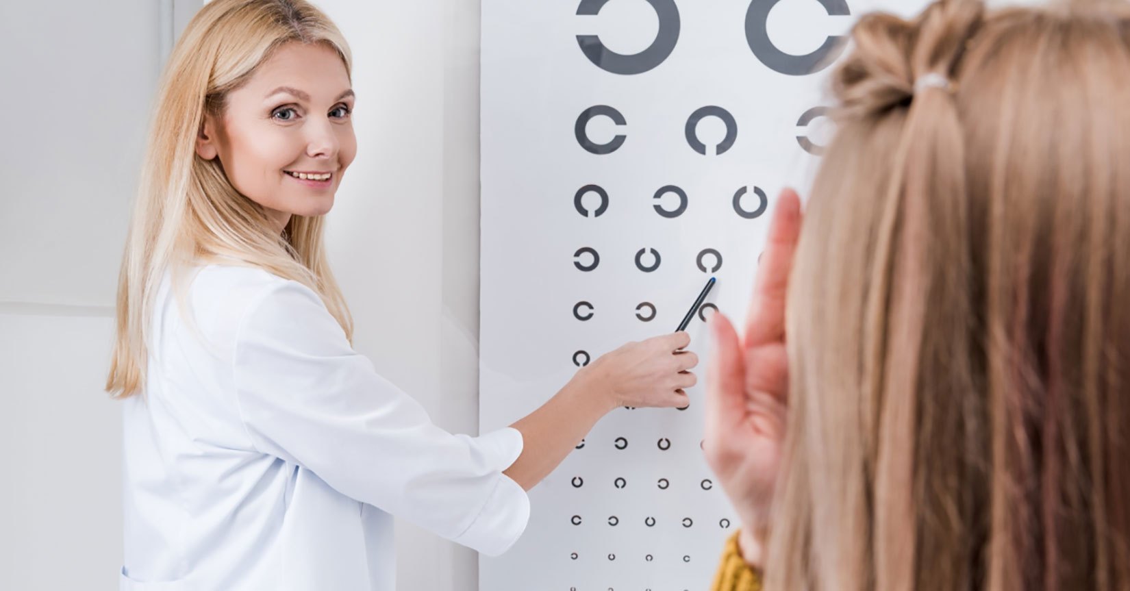 An optometrist pointing at an eye chart for a patient
