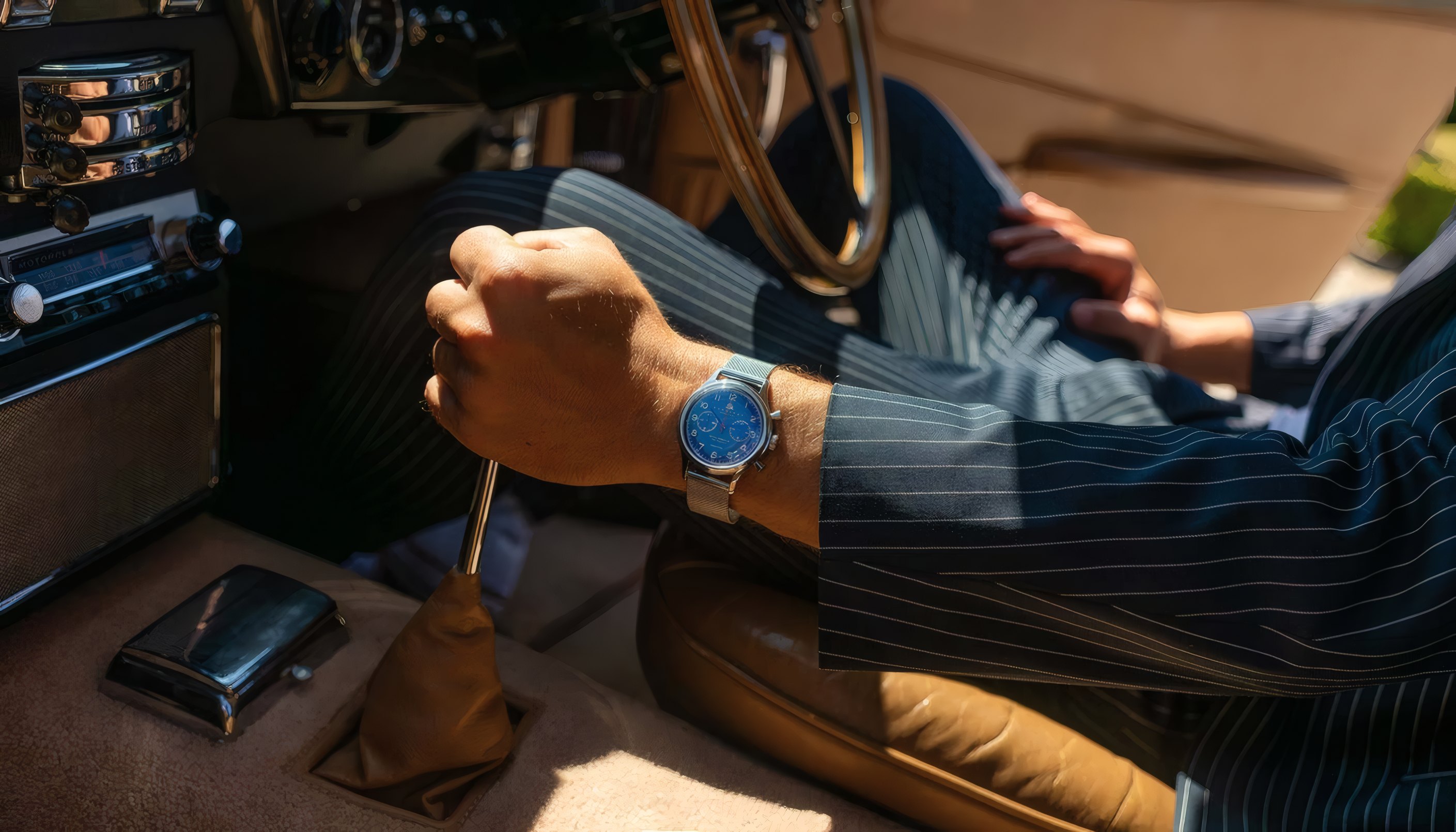 A blue-dial watch on a wrist at the wheel of a car
