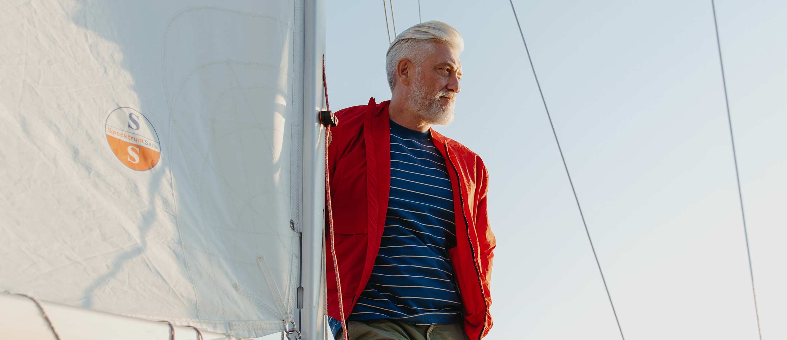 A man in a red jacket and a striped top on a sailing boat