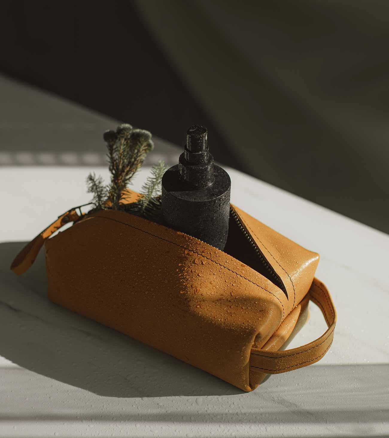 A tan leather wash bag with a black bottle