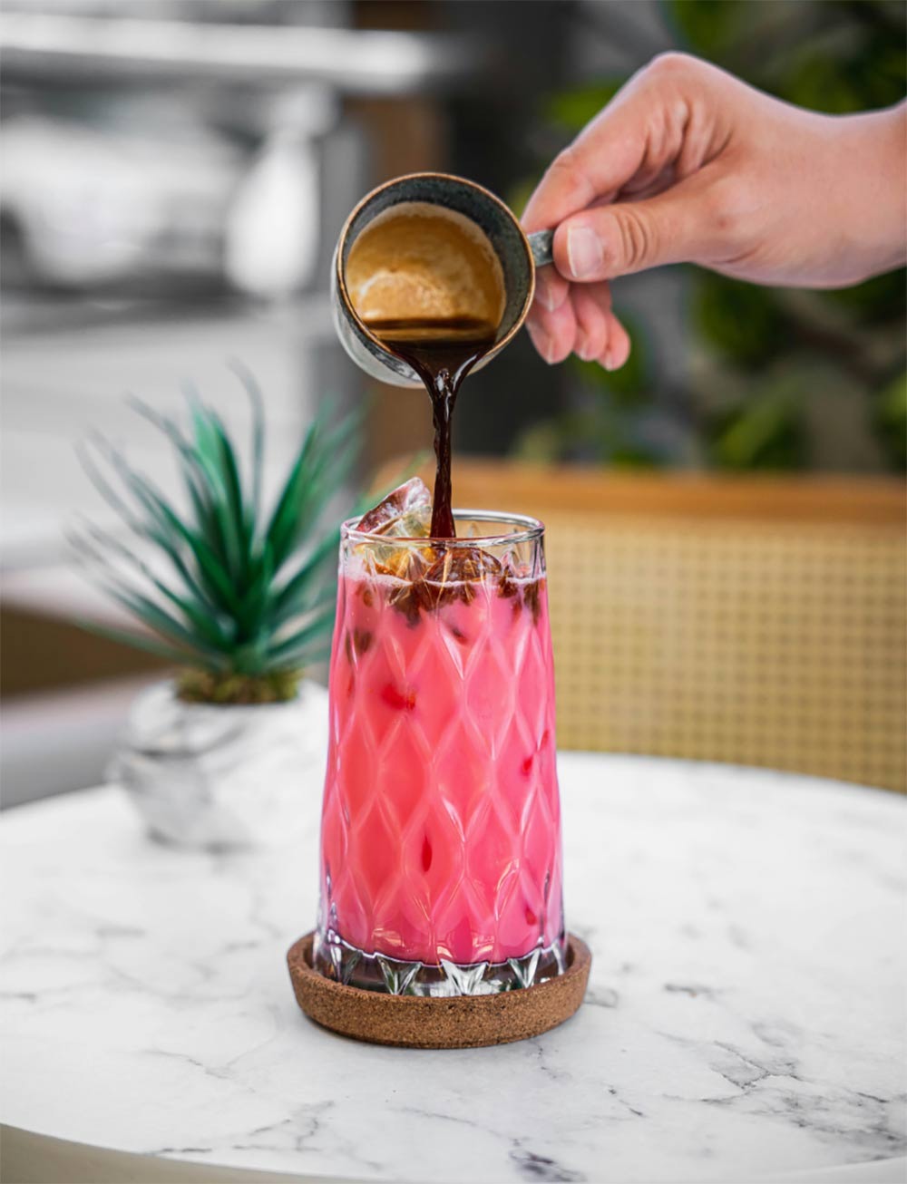A pink cocktail poured from a jigger into a crystal glass