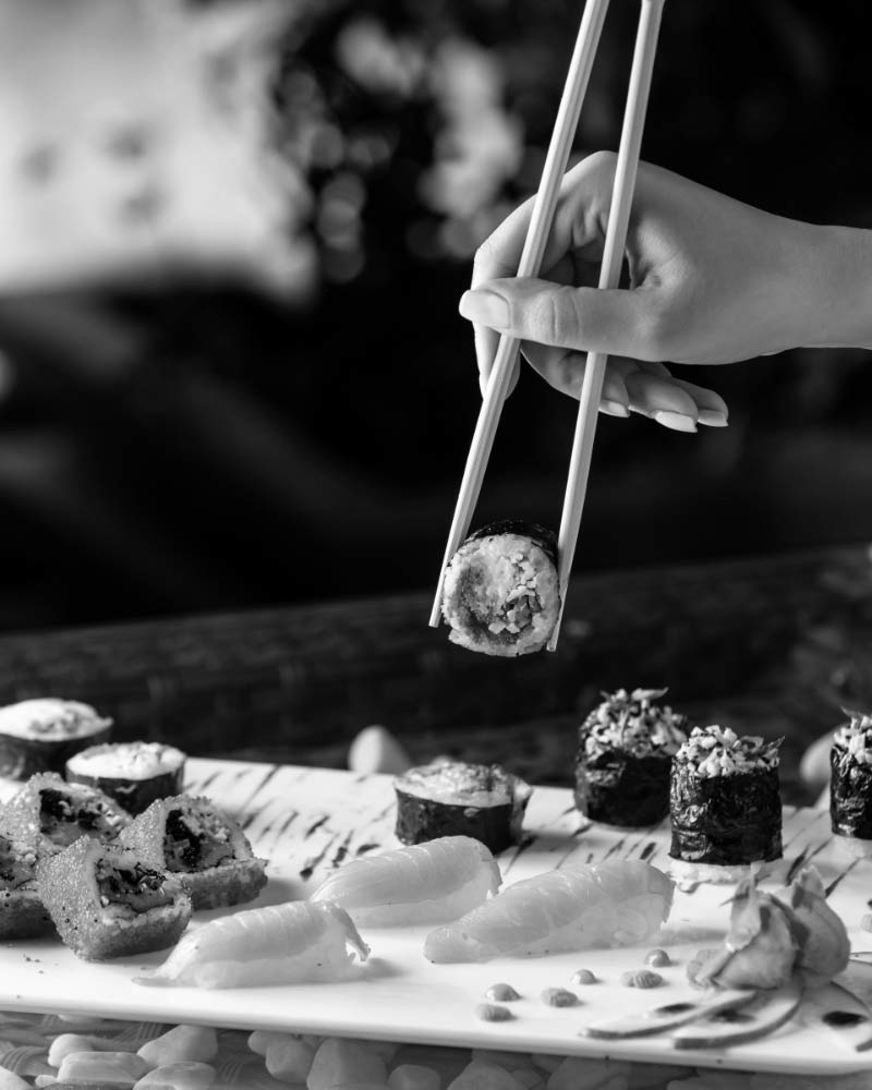 Chopsticks lifting a sushi roll, in black and white