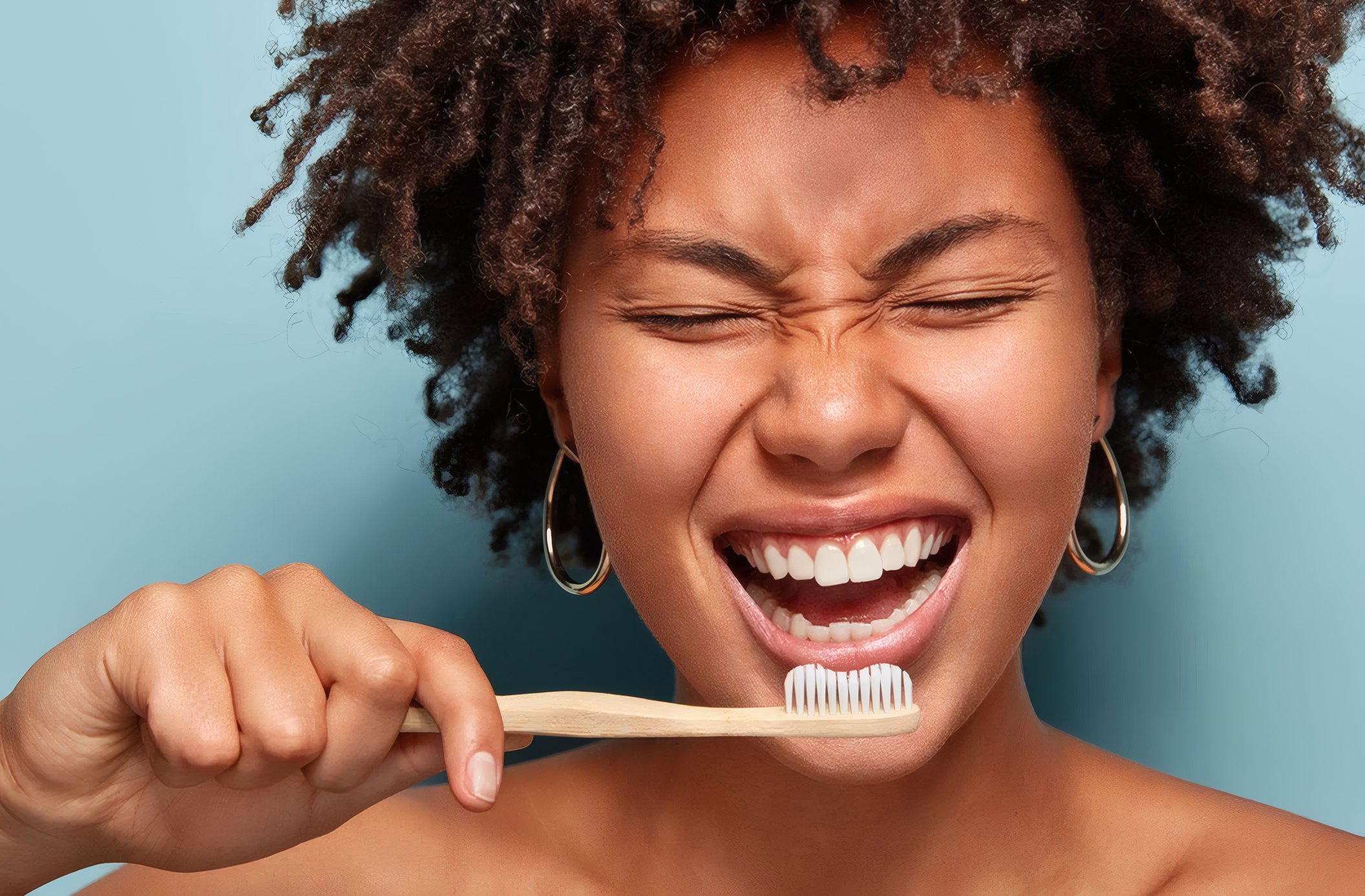 A laughing woman brushing her teeth with a bamboo toothbrush