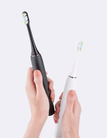 Two hands holding electric toothbrushes
