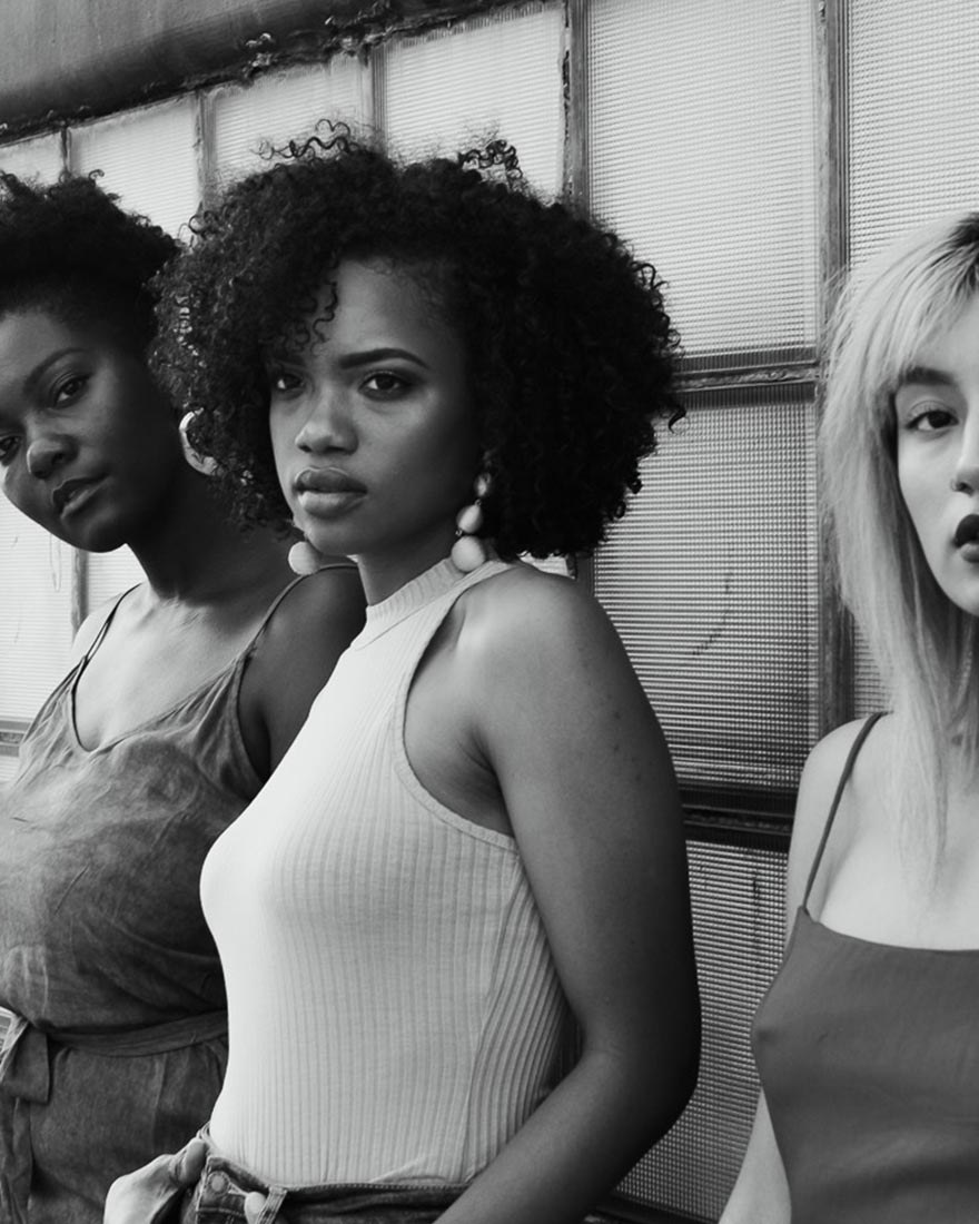 Three of our new faces against a brick wall, in black and white
