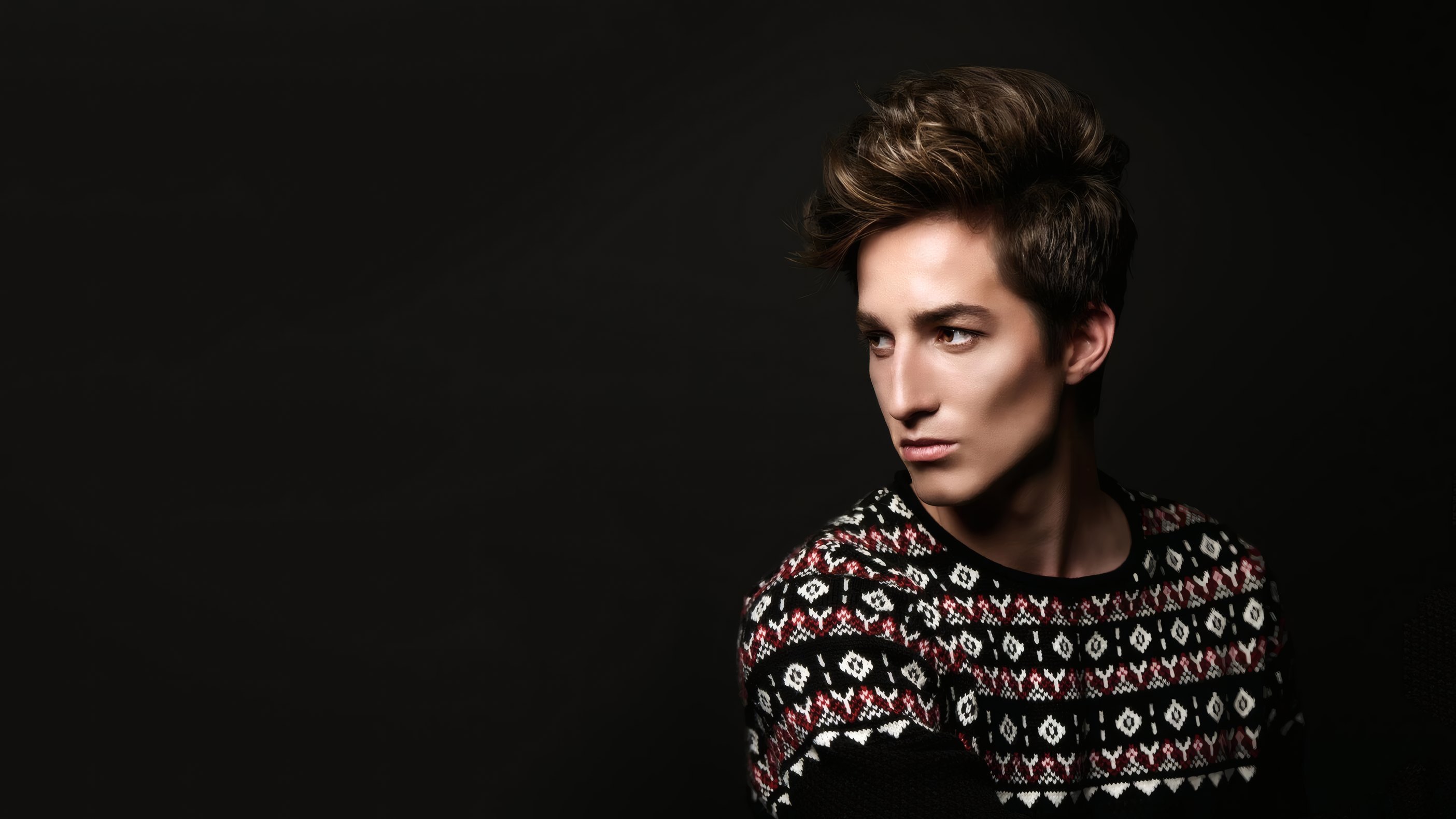 A male model in a patterned sweater against black