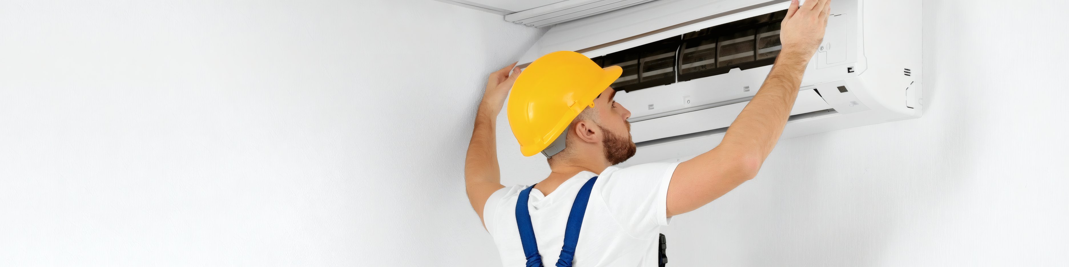 A fitter in a yellow helmet working on a wall-mounted air conditioner