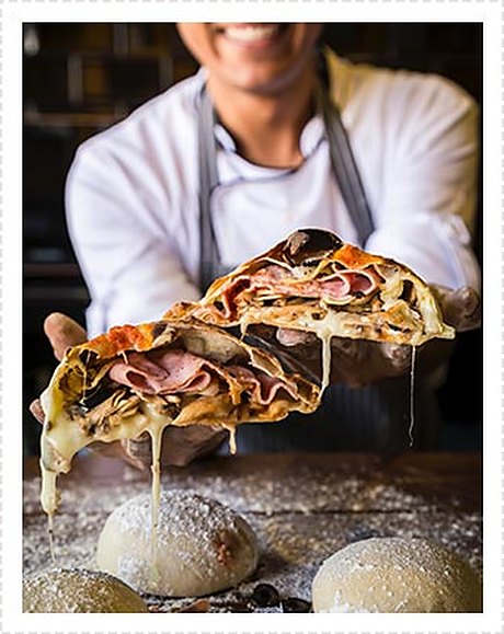 A baker holding a filled flatbread over the bench