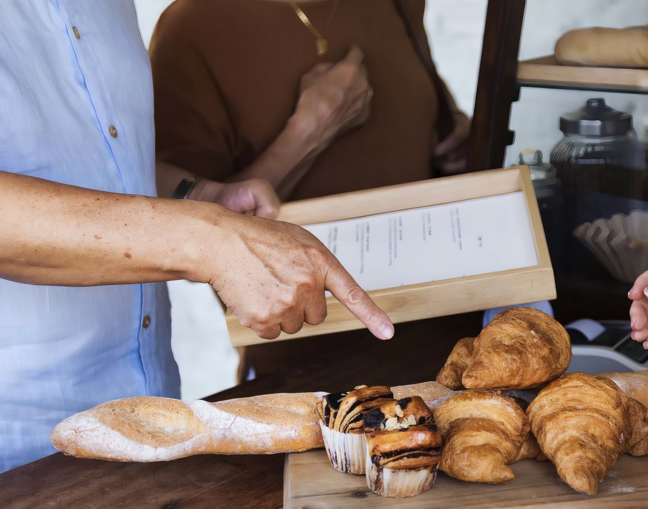 A customer pointing at the menu above a board of pastries