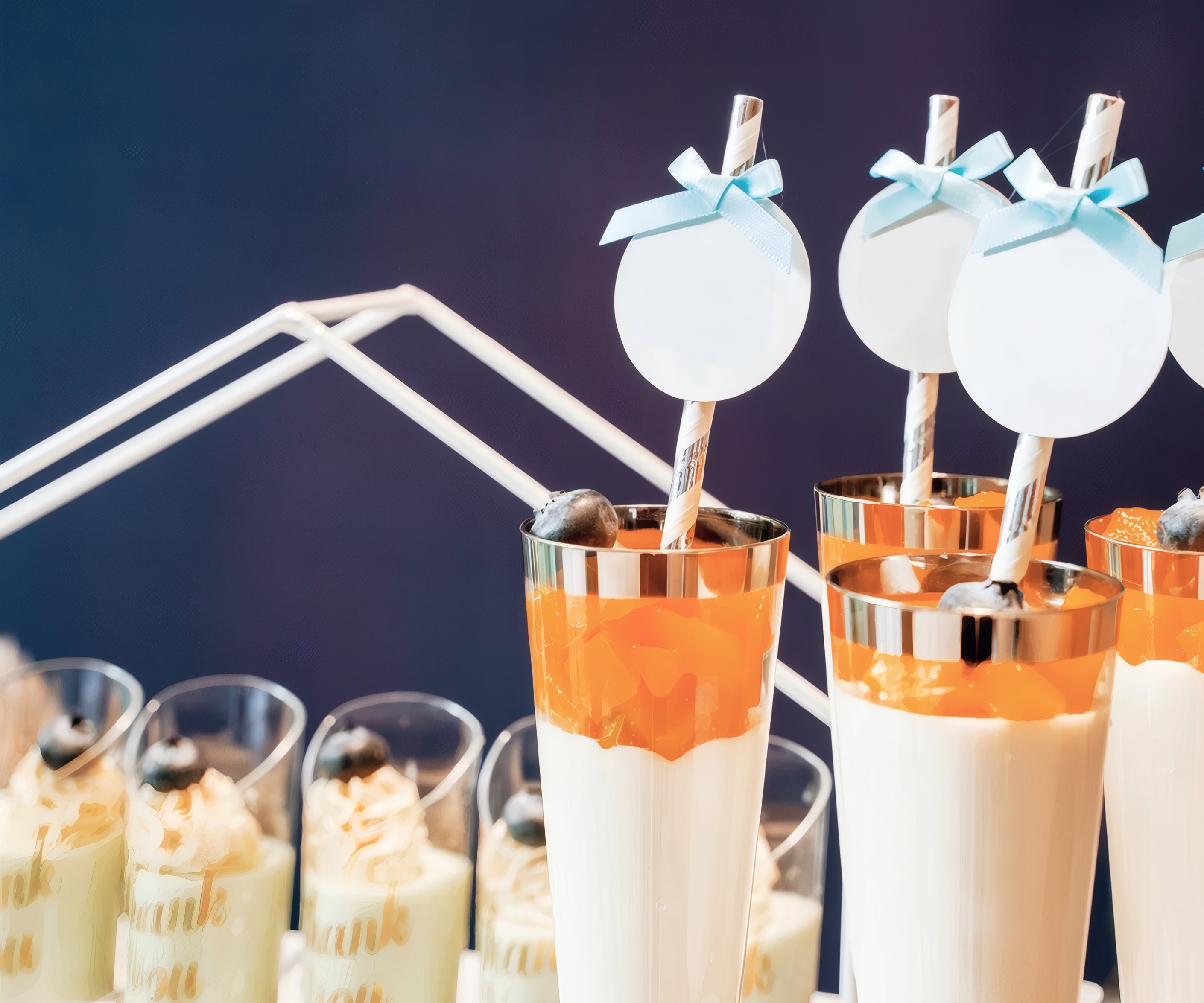 Dessert cups with paper straws and blue bows on a party table