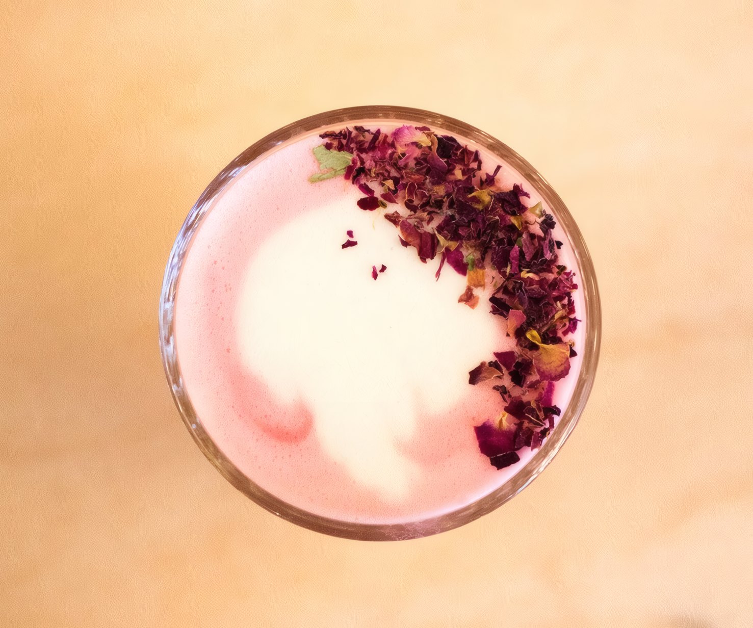 A rose milkshake topped with dried petals, seen from above