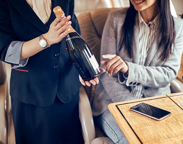 A host pouring champagne for a traveller in the cabin