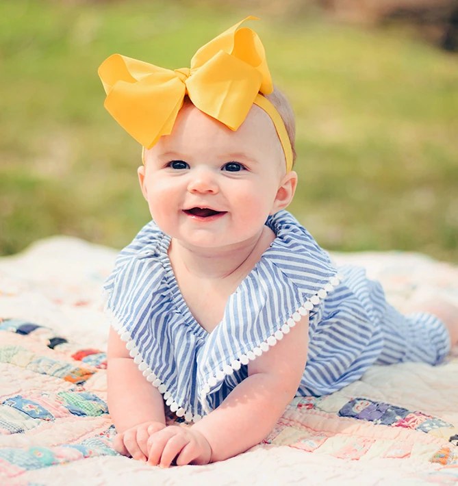 Smiling baby girl with a yellow bow lying on a quilt