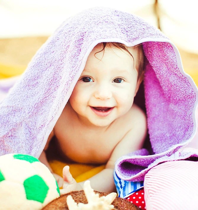 Baby peeking out from under a lilac towel