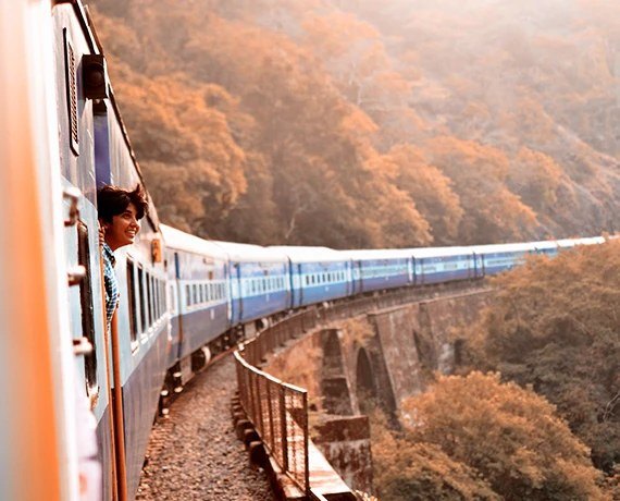 A train curving through wooded hills with a traveller at the window