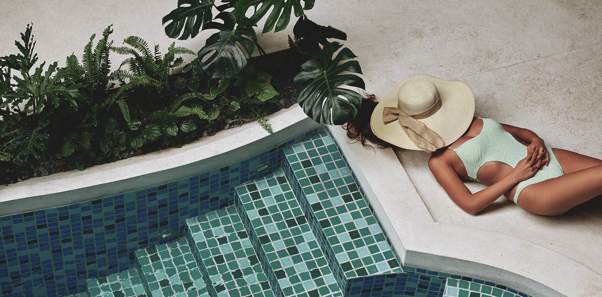 A guest in a sun hat resting by the mosaic pool