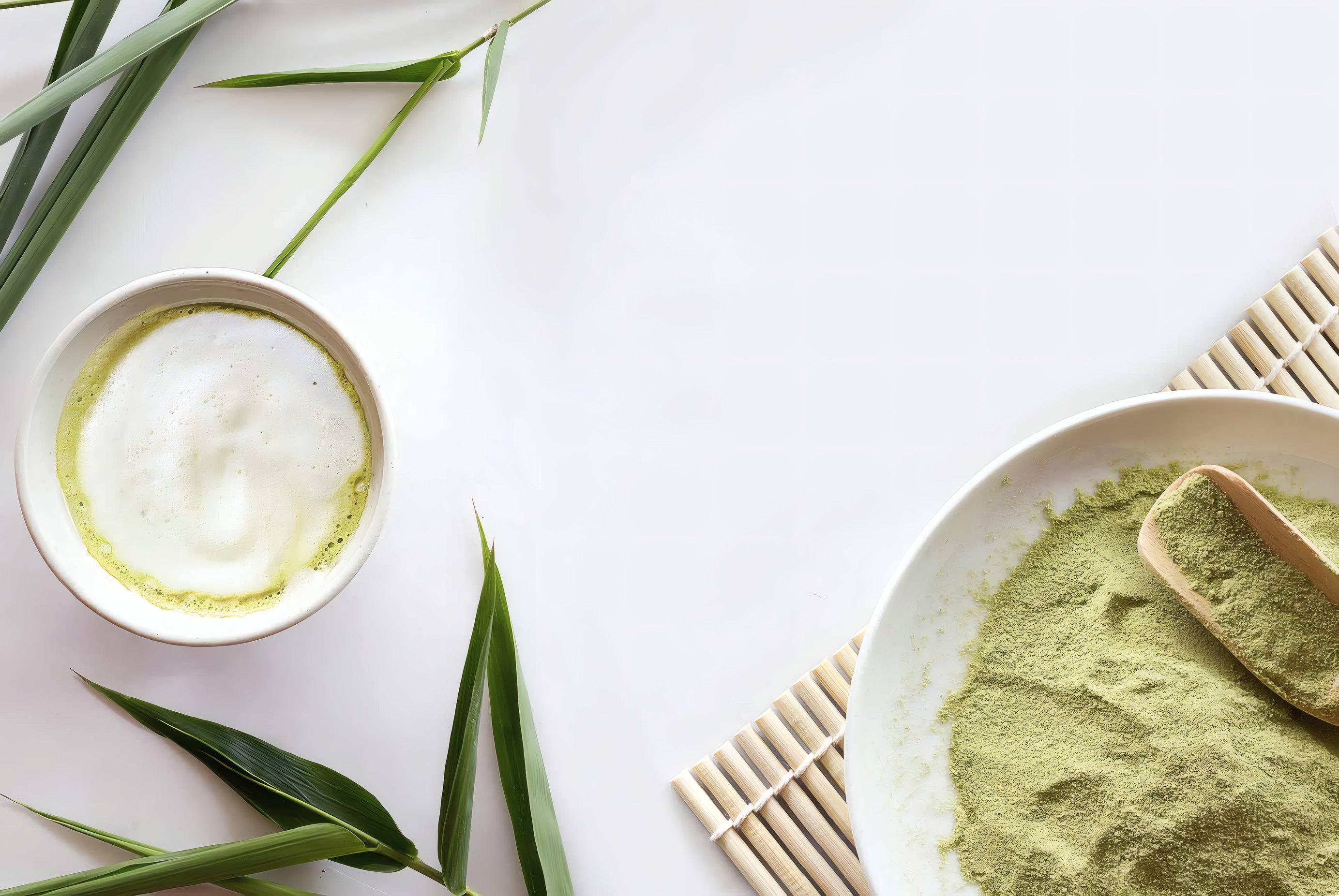 A bowl of matcha beside a dish of powdered green tea on a white table