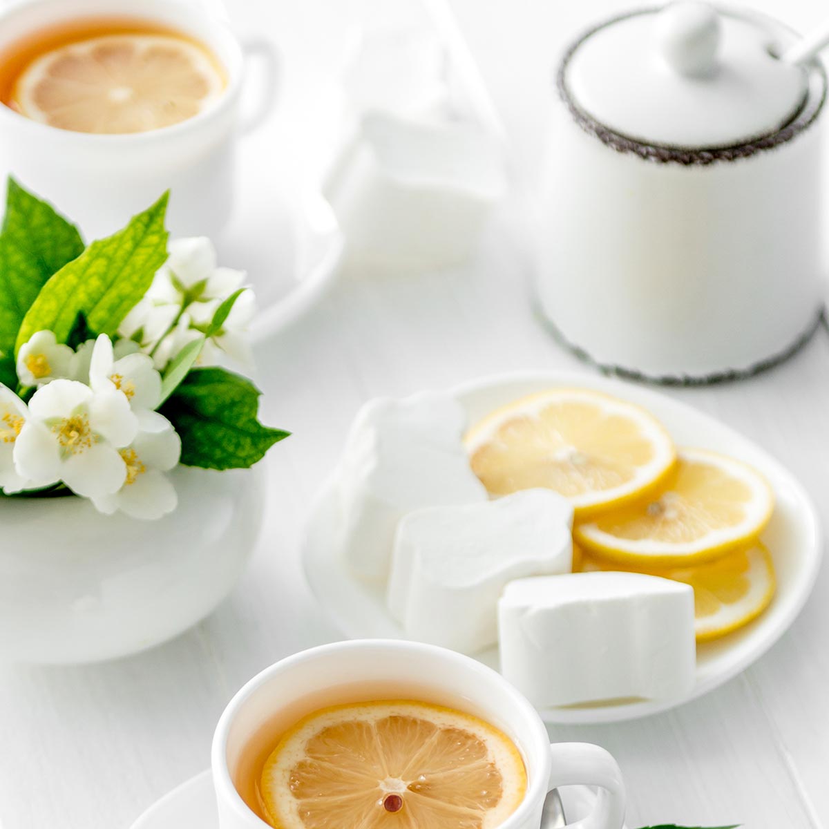 Jasmine flowers, lemon slices and a cup of tea on a white table