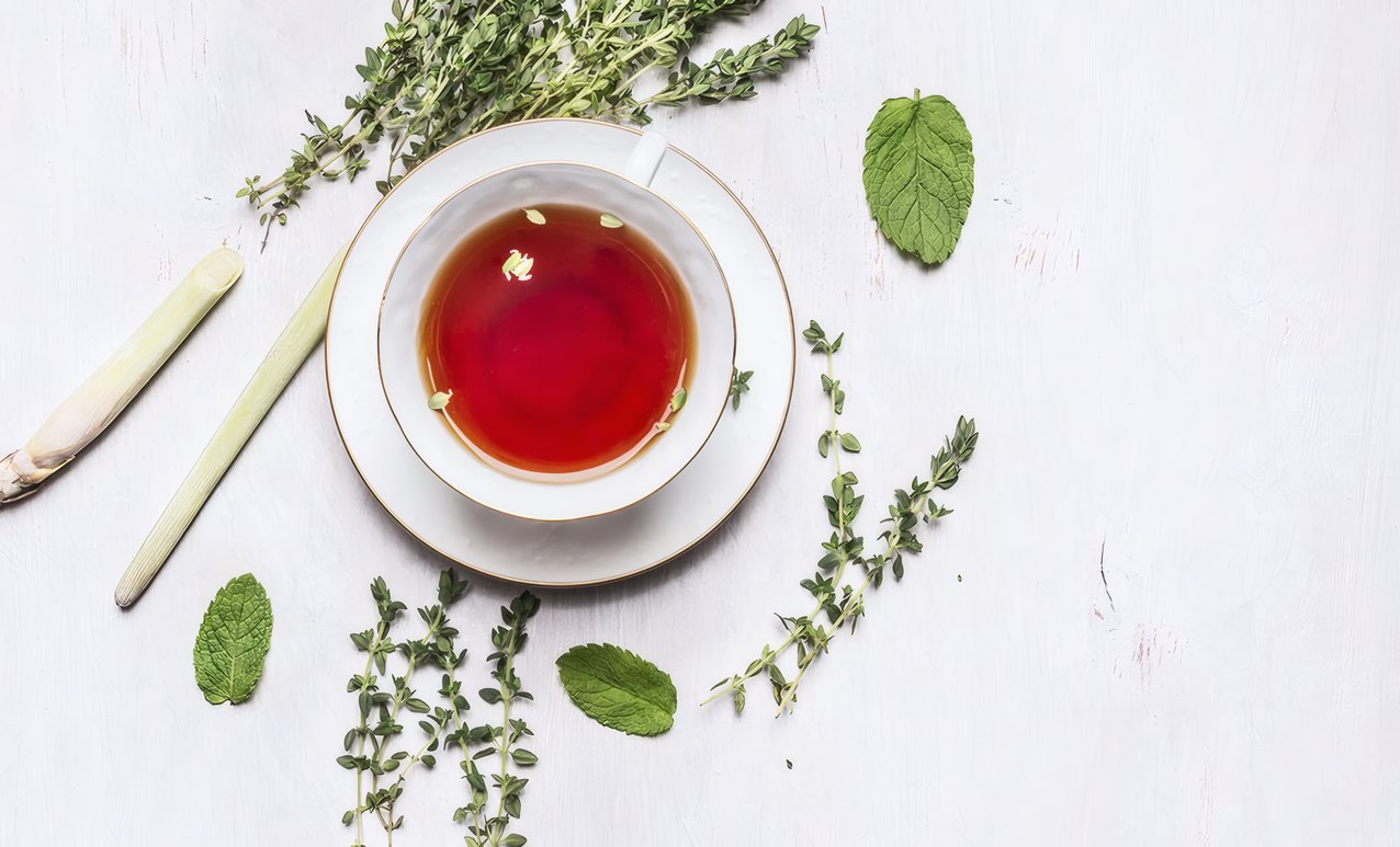 A cup of red tea surrounded by thyme and mint