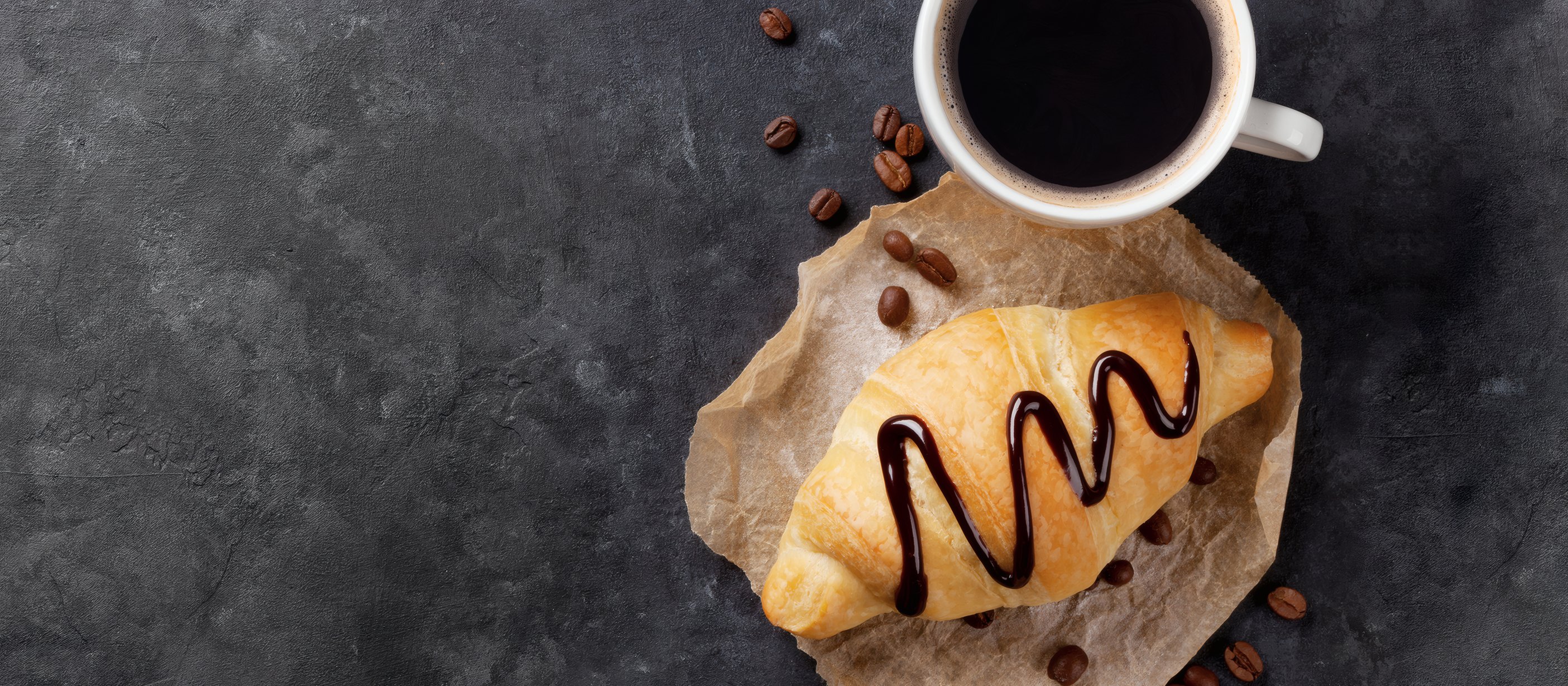 A croissant and a black coffee on dark slate