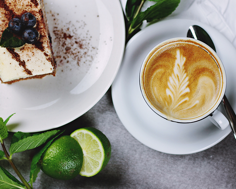 A flat white with latte art beside a slice of cake