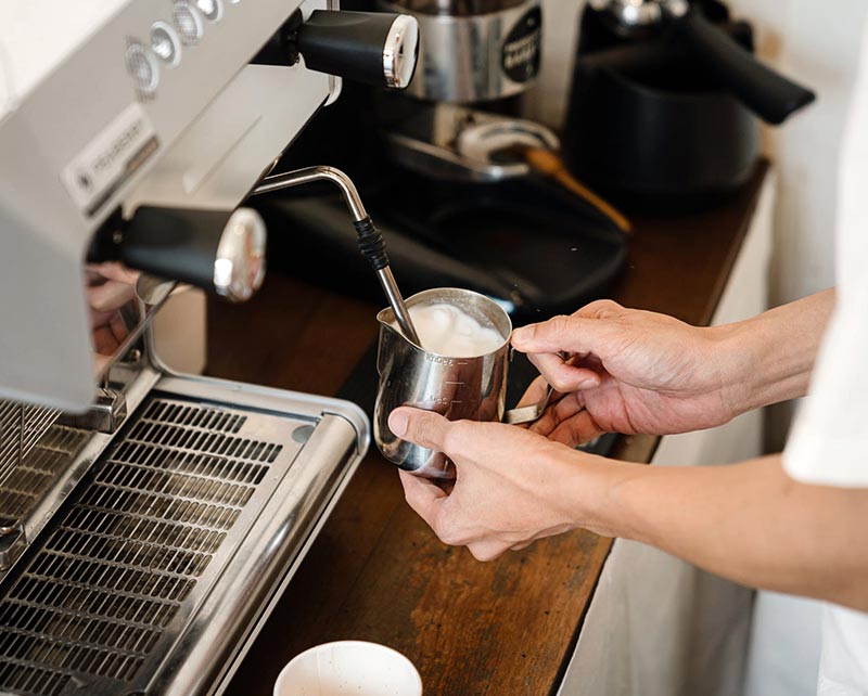 A barista pouring steamed milk at the espresso machine