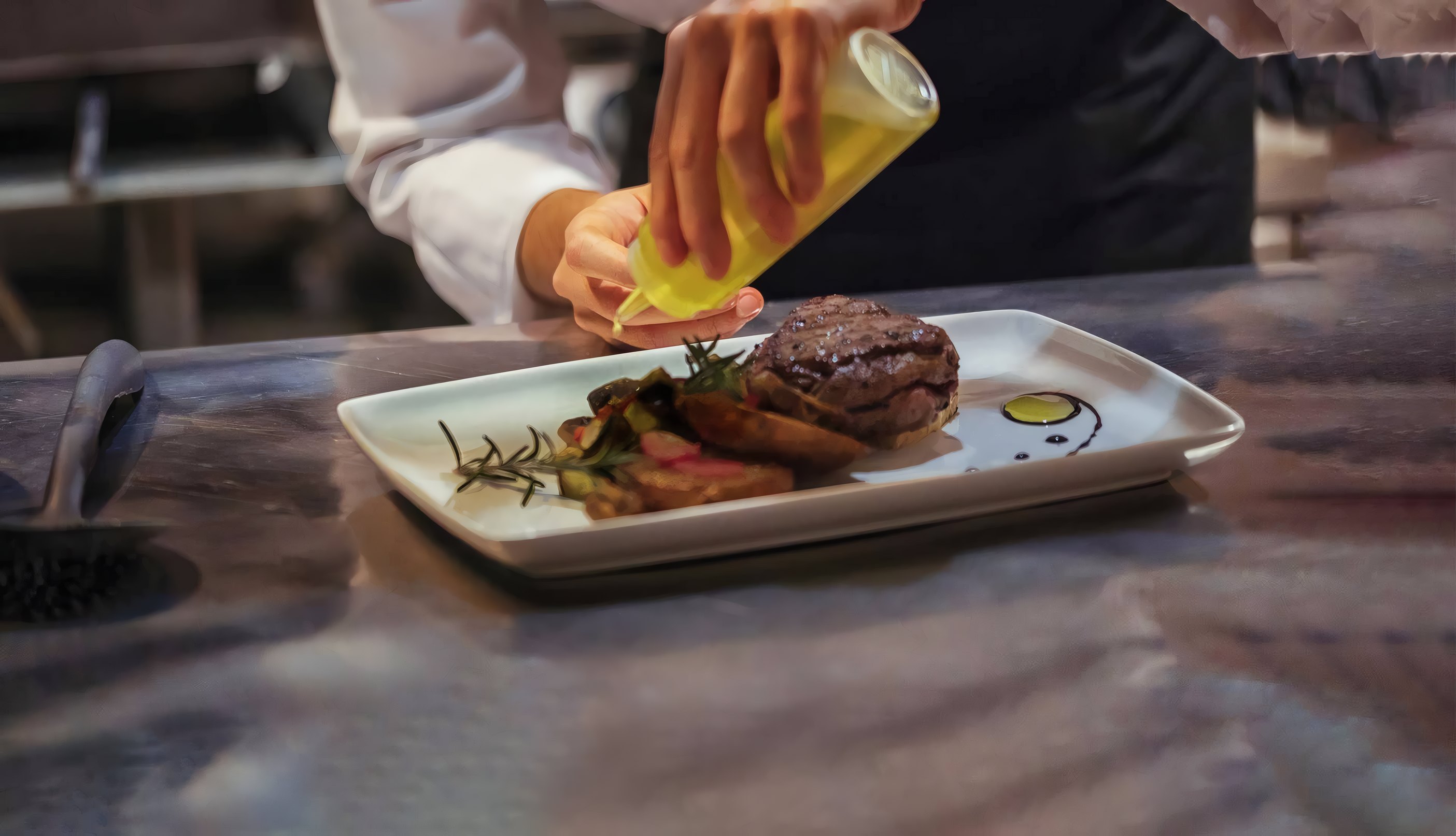 A steak being finished with sauce at the pass
