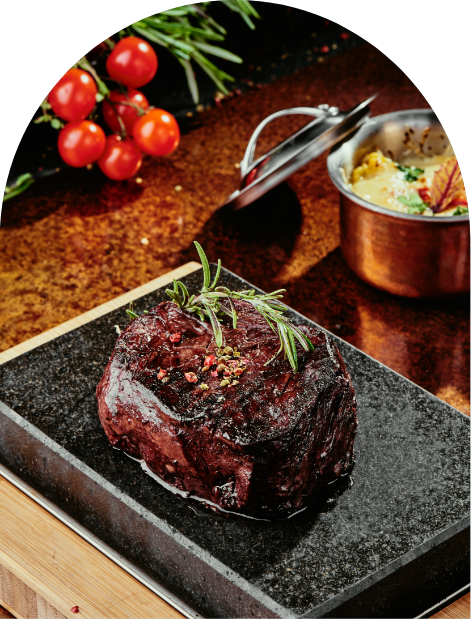 A steak on a hot stone with tomatoes and herbs