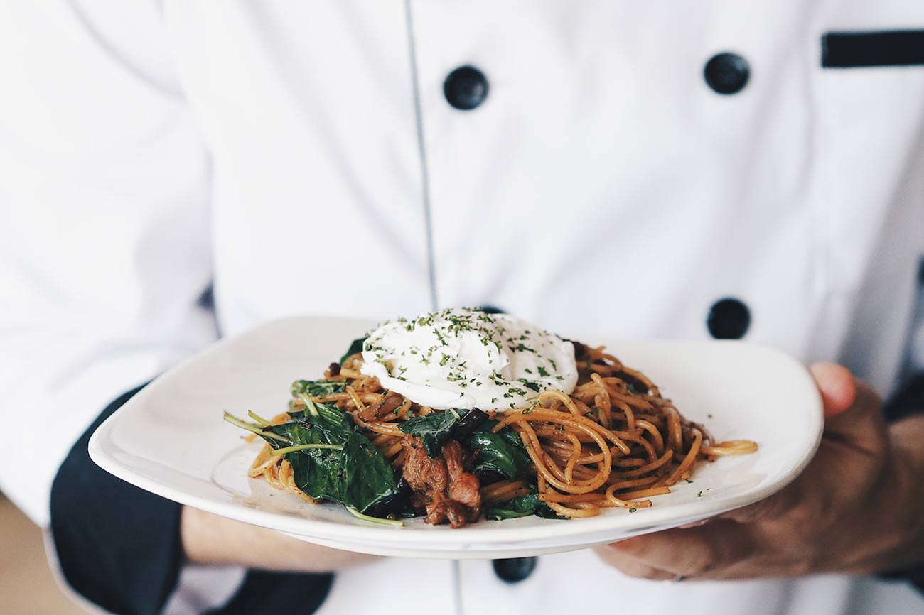 A chef in whites holding a plate of pasta