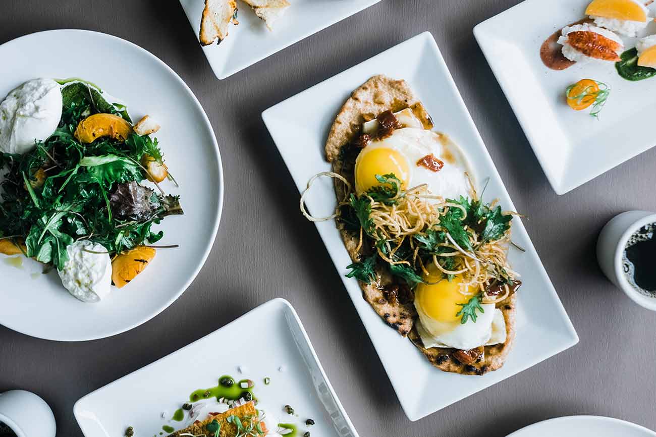 Plates of eggs, greens and fish laid out on a grey table