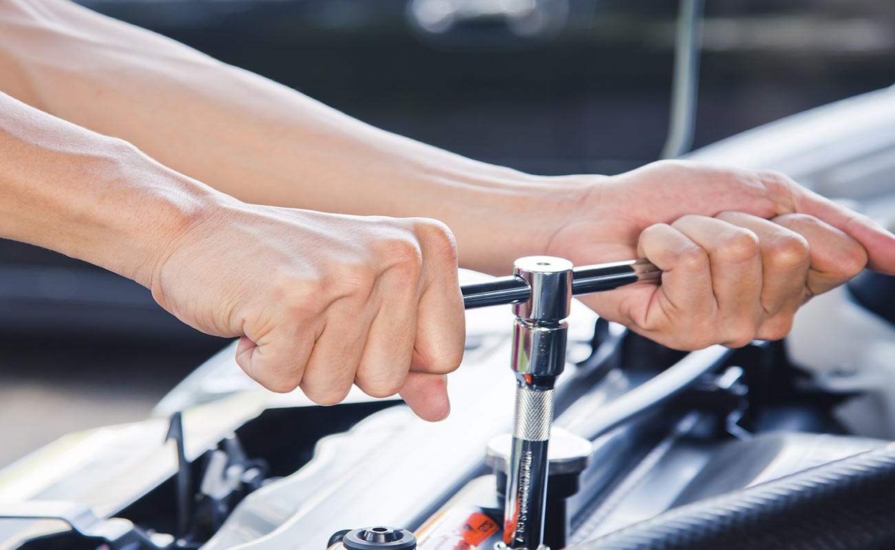 A mechanic with a ratchet in the engine bay
