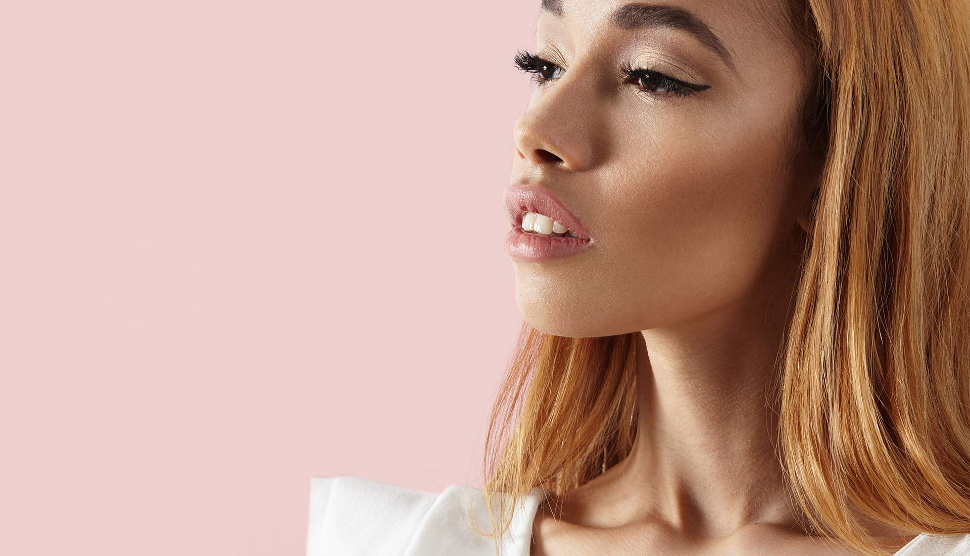 A model with a winged liner and a nude lip against a pale pink wall