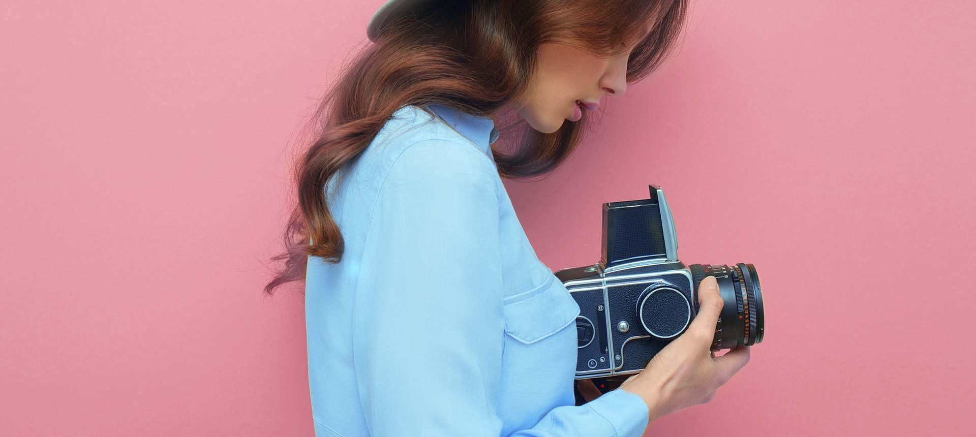 A student in a blue shirt with a medium-format camera against a pink wall