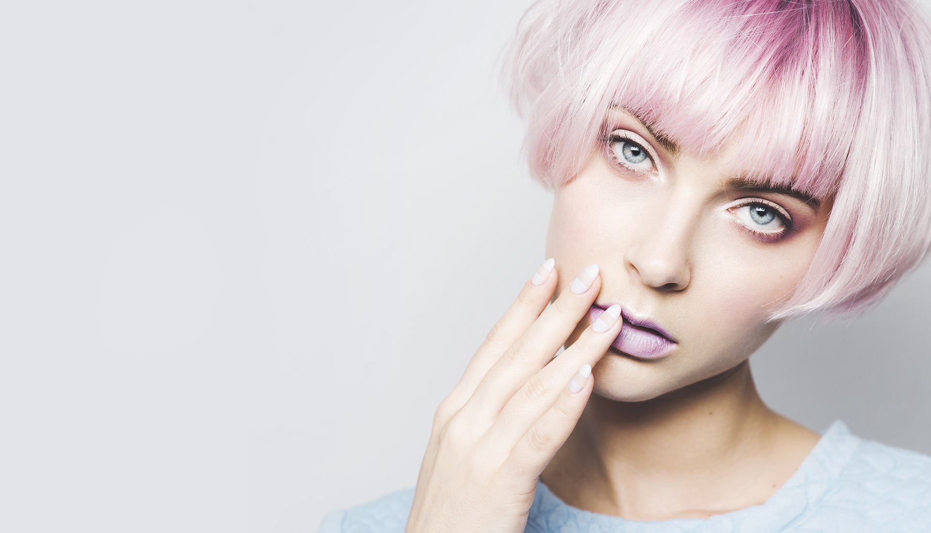 A model with a pink bob and lilac lips against a pale grey wall