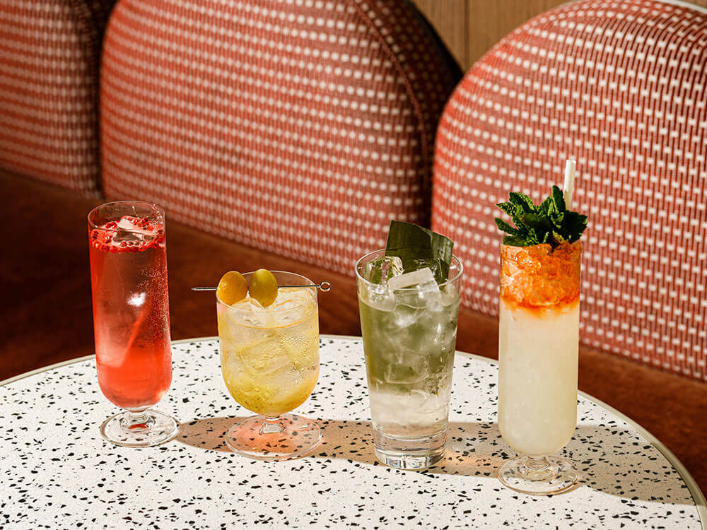 Four highballs on a terrazzo table in front of a woven banquette